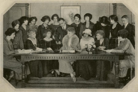 a group of fashionable people sit and stand around a table