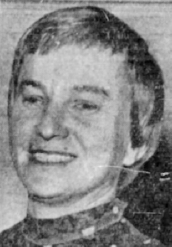 A newspaper photograph of a middle-aged white woman, smiling, with a short haircut