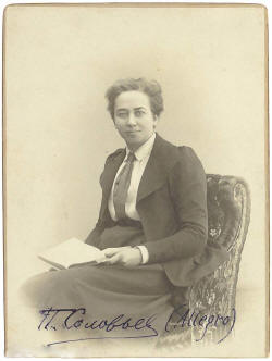 Sepia portrait of a short-haired woman wearing a jacket and long skirt, seated with a book in her lap.